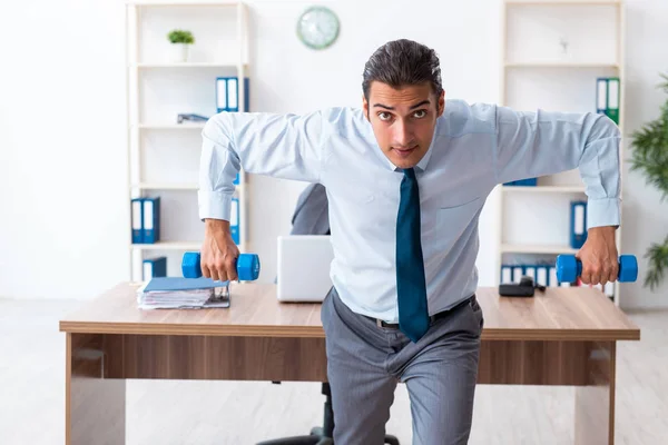 Jovem e bonito funcionário fazendo exercícios esportivos no local de trabalho — Fotografia de Stock