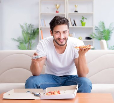 Pizza yiyen adam evde yemek yiyor, dinleniyor.