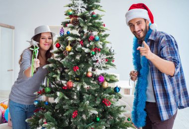 Genç aile Noel ağacını mutlu bir vesileyle süslüyor.