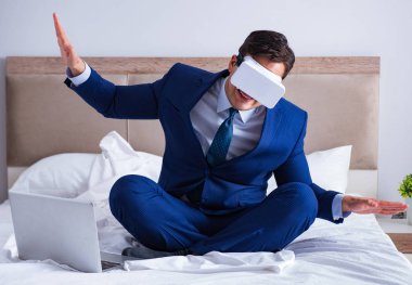 Yatak odasında sanal gerçeklik kulaklığı takan bir iş adamı.