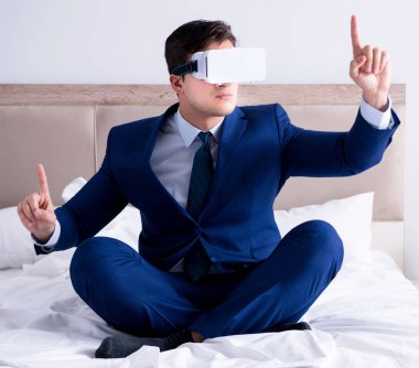 Yatak odasında sanal gerçeklik kulaklığı takan bir iş adamı.