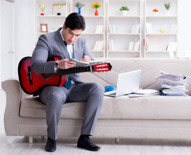Evde gitar çalan bir iş adamı.