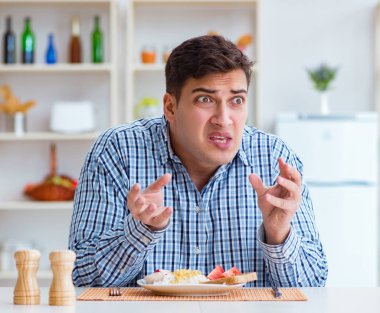 Genç koca öğle yemeğinde tatsız yemekler yiyor.