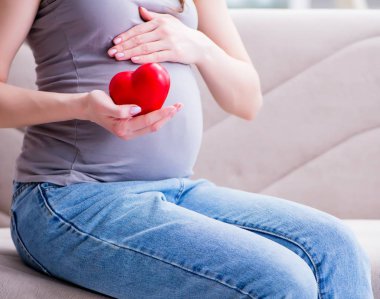 Karnında göbeği olan hamile bir kadın evdeki kanepede oturuyor.