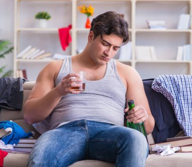 Dağınık bir odada alkol alan genç bir öğrenci.