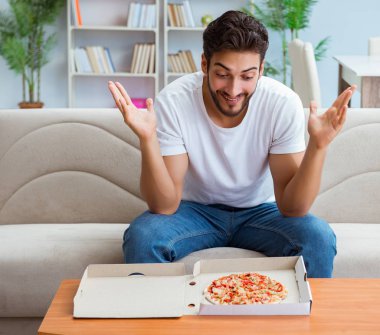 Pizza yiyen adam evde yemek yiyor, dinleniyor.