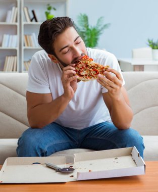 Pizza yiyen adam evde yemek yiyor, dinleniyor.