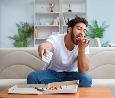 Pizza yiyen adam evde yemek yiyor, dinleniyor.