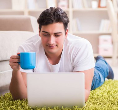 Evde, halı döşemesinde dizüstü bilgisayarda çalışan adam.