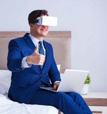 Yatak odasında sanal gerçeklik kulaklığı takan bir iş adamı.