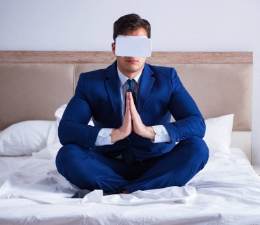 Yatak odasında sanal gerçeklik kulaklığı takan bir iş adamı.