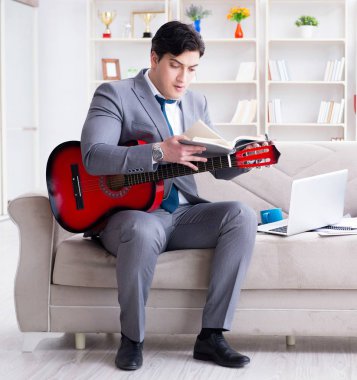 Evde gitar çalan bir iş adamı.