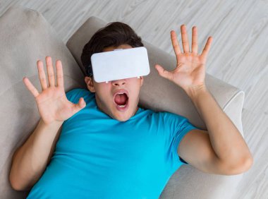 VR gözlüklü genç adam kanepede dinleniyor.