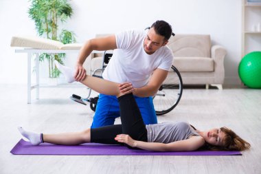 Erkek fizyoterapist yerde yaralı bir kadınla egzersiz yapıyor.