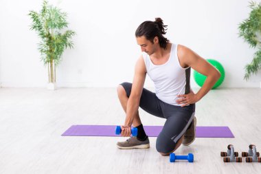 Genç yakışıklı adam içeride spor yapıyor.