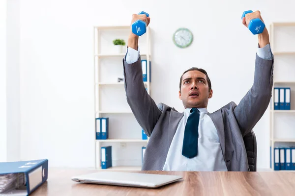 Jovem e bonito funcionário fazendo exercícios esportivos no local de trabalho — Fotografia de Stock