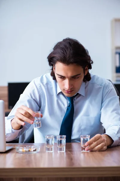 Male employee drinking vodka and smoking cigarettes at workplace