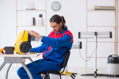 Genç erkek müteahhit atölyede elektrik süpürgesi tamir ediyor.