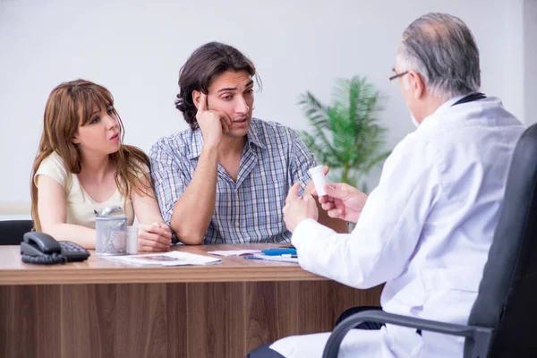 Pareja joven visitando viejo médico masculino — Foto de Stock