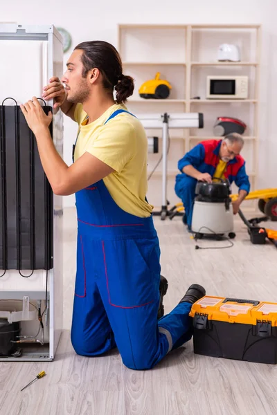 Two contractors repairing fridge at workshop