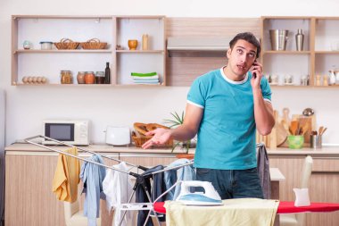 Genç adam evde çamaşır ütülüyor.