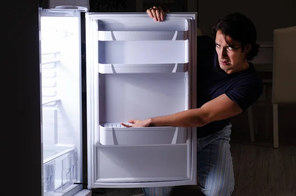 Muž lámání stravy v noci v blízkosti lednice — Stock fotografie