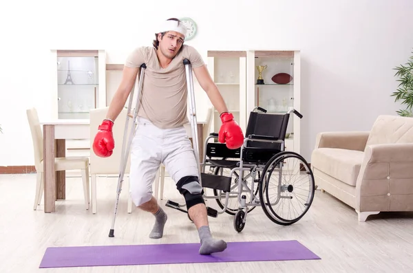 Jovem ferido fazendo exercícios em casa — Fotografia de Stock