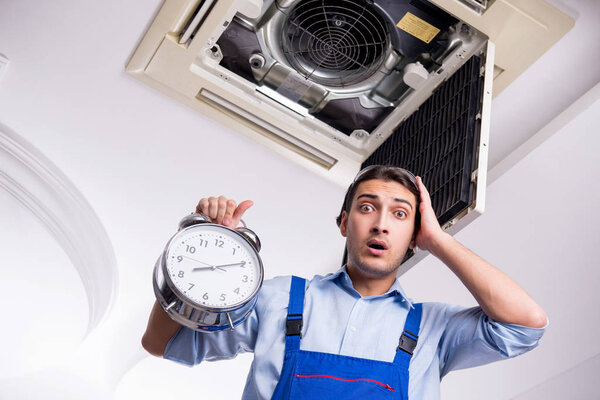 Молодой ремонтник ремонтирует потолочные кондиционеры