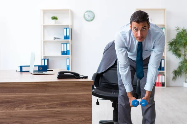 Young handsome employee doing sport exercises at workplace — Stock Photo, Image