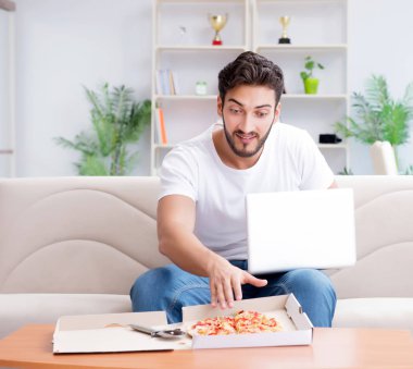 Pizza yiyen adam evde yemek yiyor, dinleniyor.