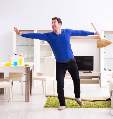 Genç adam yerleri süpürgeyle temizliyor.