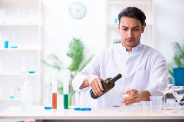 Erkek kimyager laboratuvarda şarap örneklerini inceliyor.