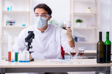 Male chemist examining wine samples at lab clipart