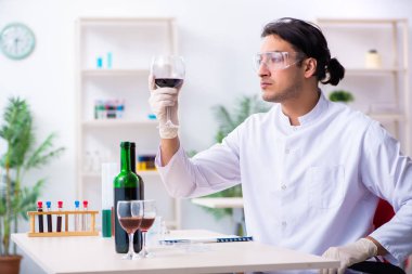 Erkek kimyager laboratuvarda şarap örneklerini inceliyor.