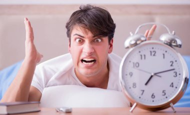 Yataktaki adam alarm yüzünden uykusuzluk çekiyor.