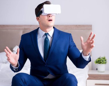 Yatak odasında sanal gerçeklik kulaklığı takan bir iş adamı.