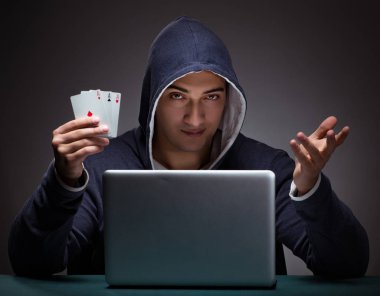 Kapüşonlu genç adam dizüstü bilgisayarın önünde oturuyor.