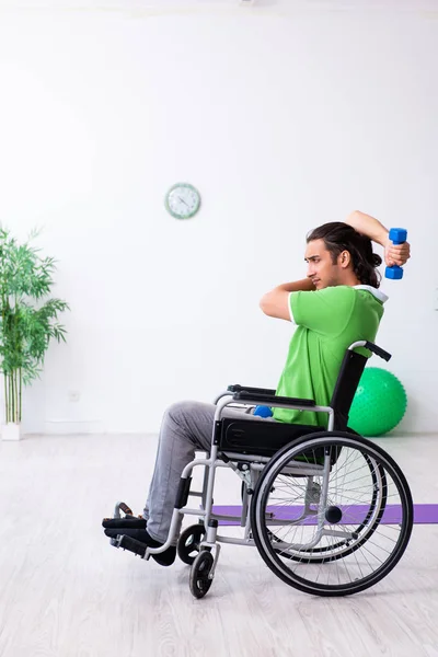 Jovem em cadeira de rodas fazendo exercícios dentro de casa — Fotografia de Stock