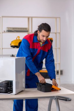 Genç müteahhit atölyede buzdolabını tamir ediyor.