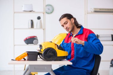 Genç erkek müteahhit atölyede elektrik süpürgesi tamir ediyor.