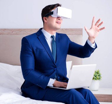 Yatak odasında sanal gerçeklik kulaklığı takan bir iş adamı.