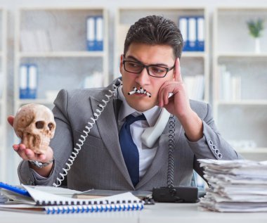 Ofisteki işadamı elinde insan kafatasıyla sigara içiyor.