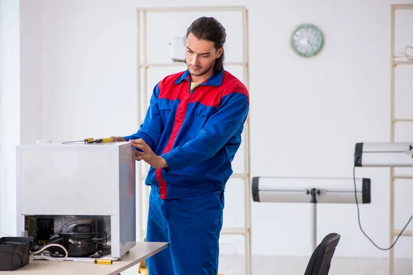 Young male contractor repairing refrigerator at workshop — Stock Photo, Image
