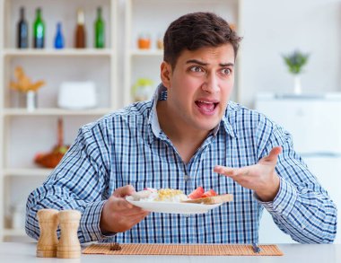 Genç koca öğle yemeğinde tatsız yemekler yiyor.