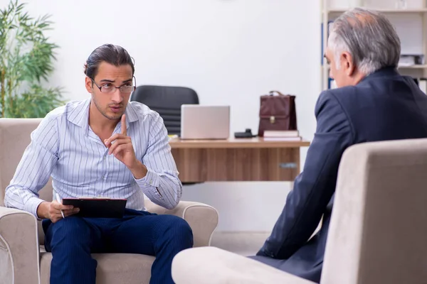 Oude man op bezoek bij jonge mannelijke dokter psycholoog — Stockfoto