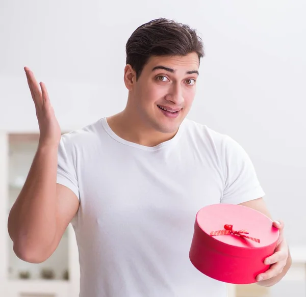 Der junge Mann mit Geschenktüte zu Hause bereitet Überraschung für Frau vor — Stockfoto