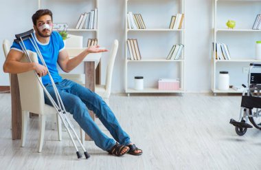 Genç adam ameliyattan sonra koltuk değnekleriyle evde iyileşiyor.
