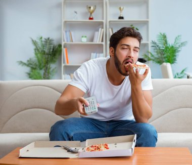 Pizza yiyen adam evde yemek yiyor, dinleniyor.