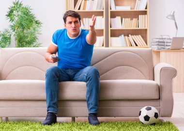 Evdeki kanepede oturup futbol izleyen bir adam.