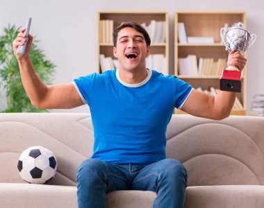Evdeki kanepede oturup futbol izleyen bir adam.